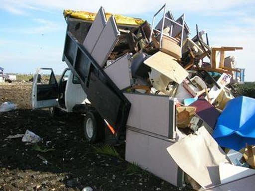 *   Image content: A white dump truck with its bed tilted up, spilling a large pile of furniture and household debris onto a