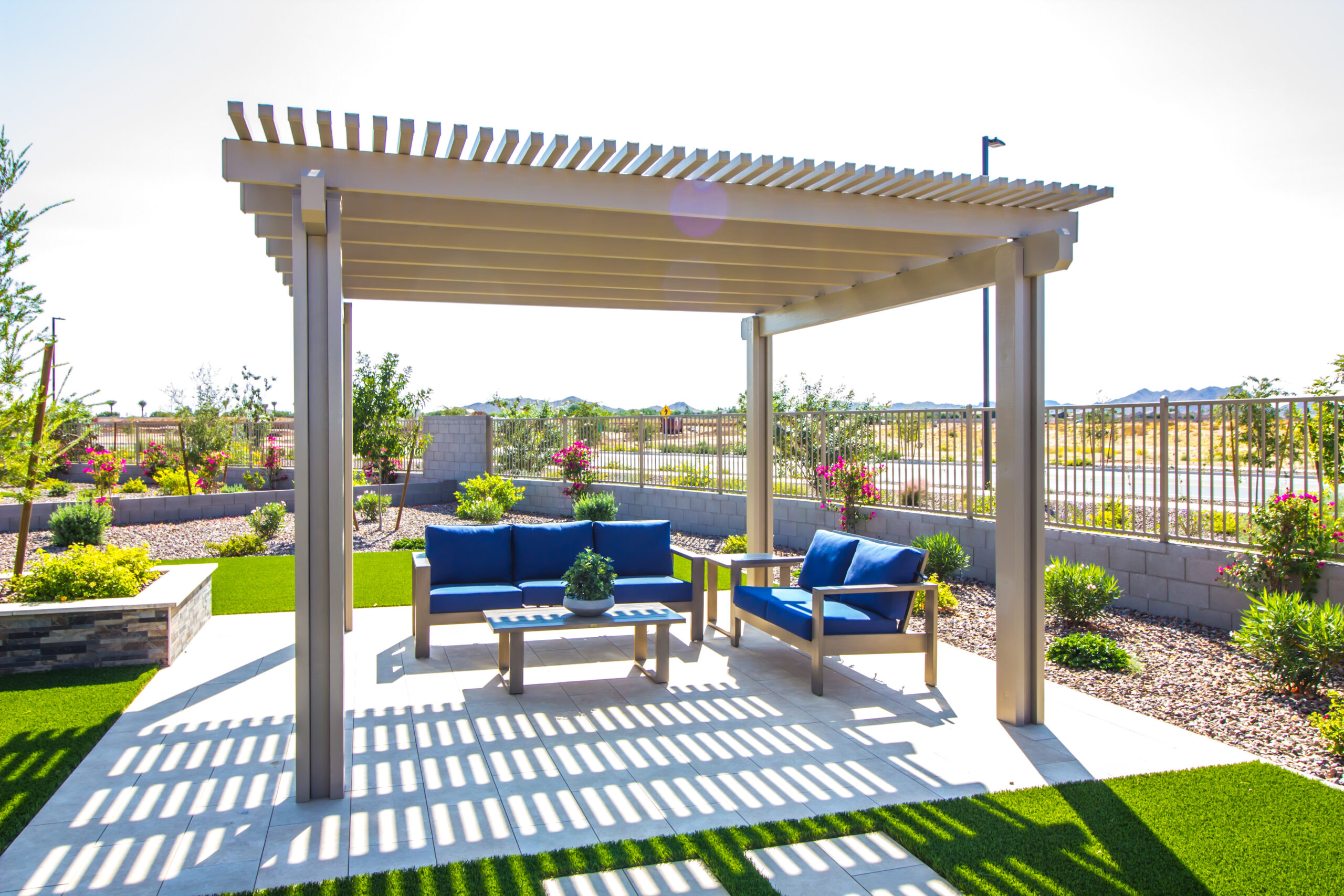 Modern patio with blue outdoor sofas and a coffee table shaded by a tan pergola on a tiled floor.