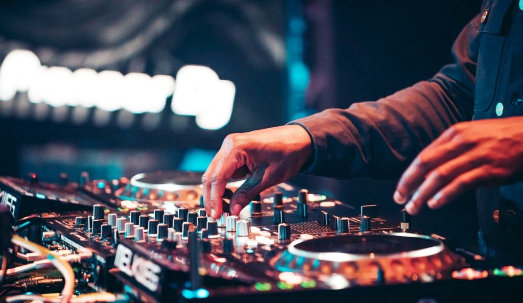 DJ's hands adjusting knobs and settings on a professional Pioneer DJ mixing console in a dimly lit club.