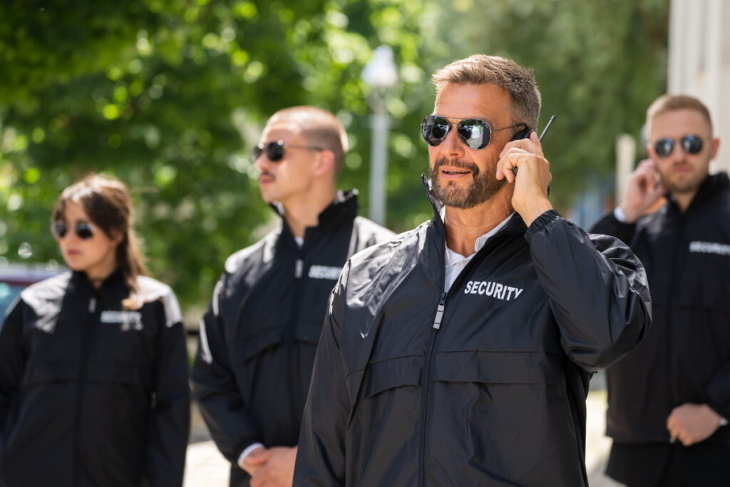 Security guards in black uniforms and sunglasses, with one man in the foreground talking on a walkie-talkie.