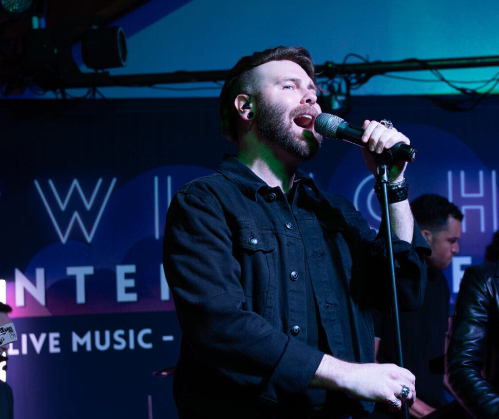 Bearded male singer in a black shirt performing on stage under blue lighting.