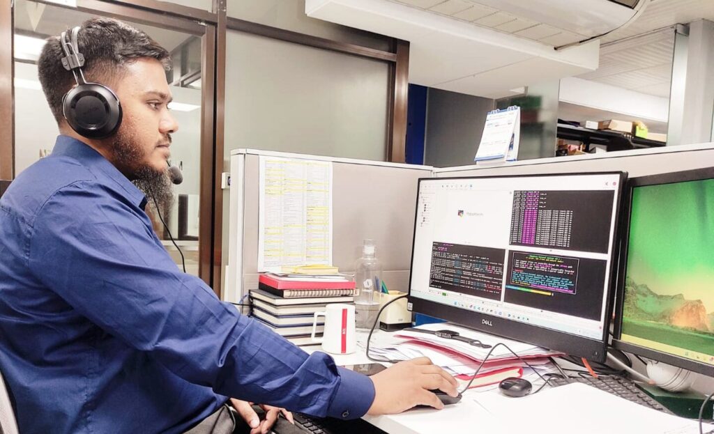 Man with a beard and headset working at a computer desk with dual monitors displaying code.