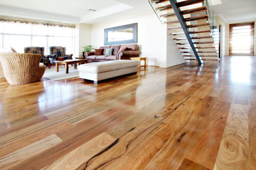 Modern living room with polished hardwood floors, brown leather sofa, and open floating staircase.