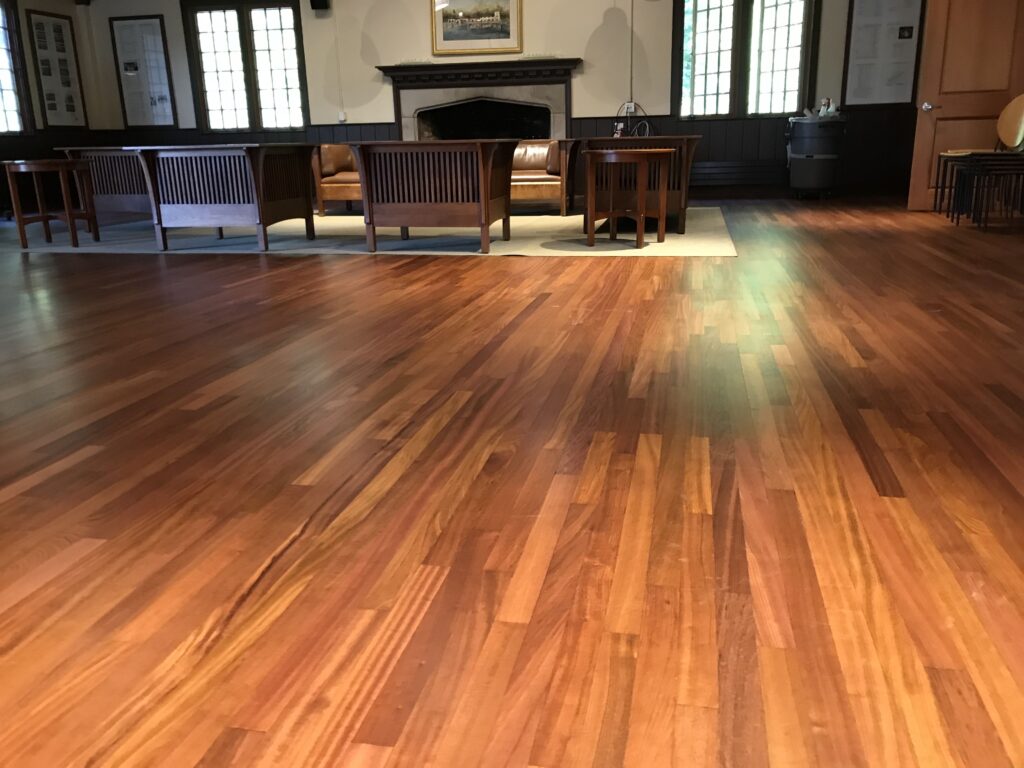 Polished hardwood floors in a spacious room with a wooden seating area and a fireplace in the background.