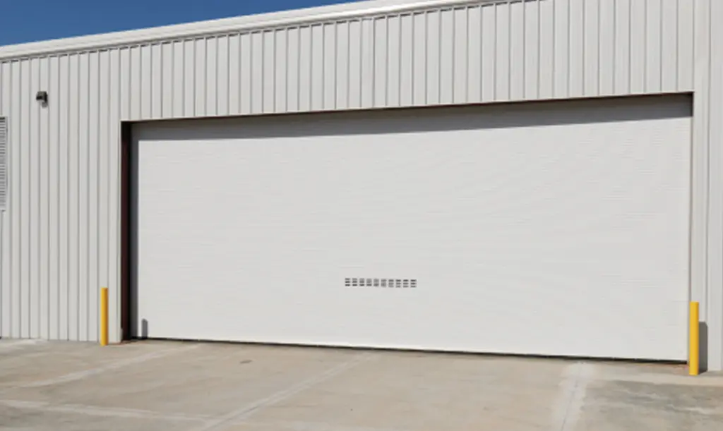 Large white roll-up door on a corrugated metal warehouse building with yellow safety bollards.