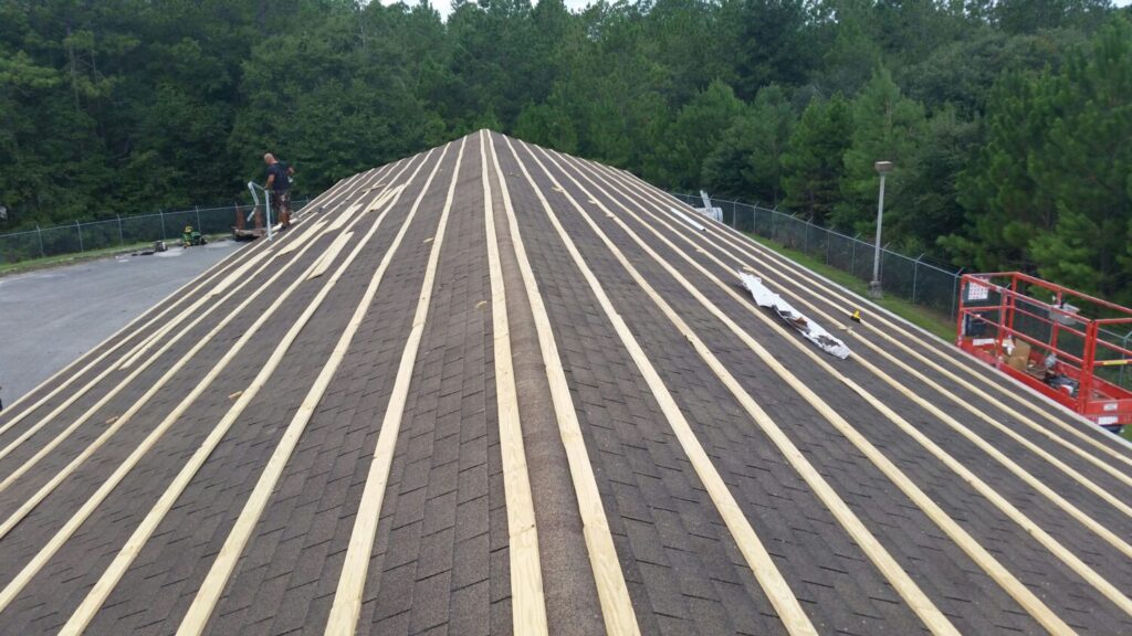 Vertical wooden battens being installed over a dark shingled peaked roof.