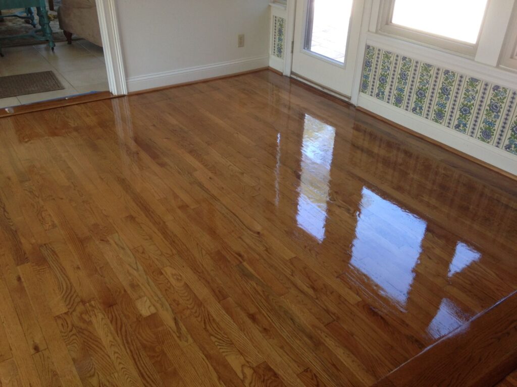Freshly polished, light brown hardwood floors reflecting light from a glass door and window.