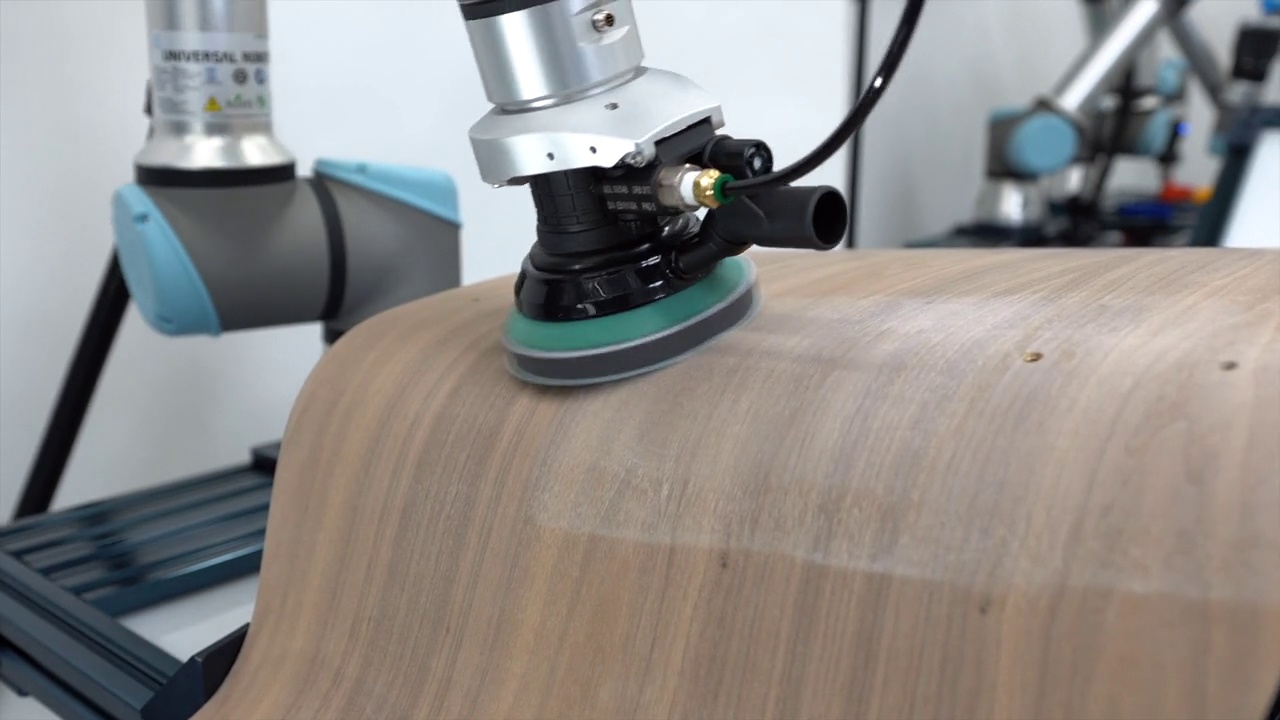 Robotic arm using a rotating sanding disc to smooth a curved wooden surface.