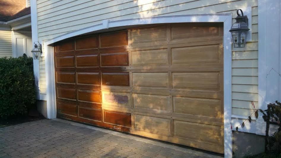 Half-finished wooden garage door showing a contrast between the original dark stained wood and the sanded, lighter surface.