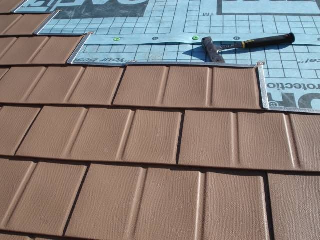 Brown roof shingles being installed over blue underlayment with a hammer resting nearby.