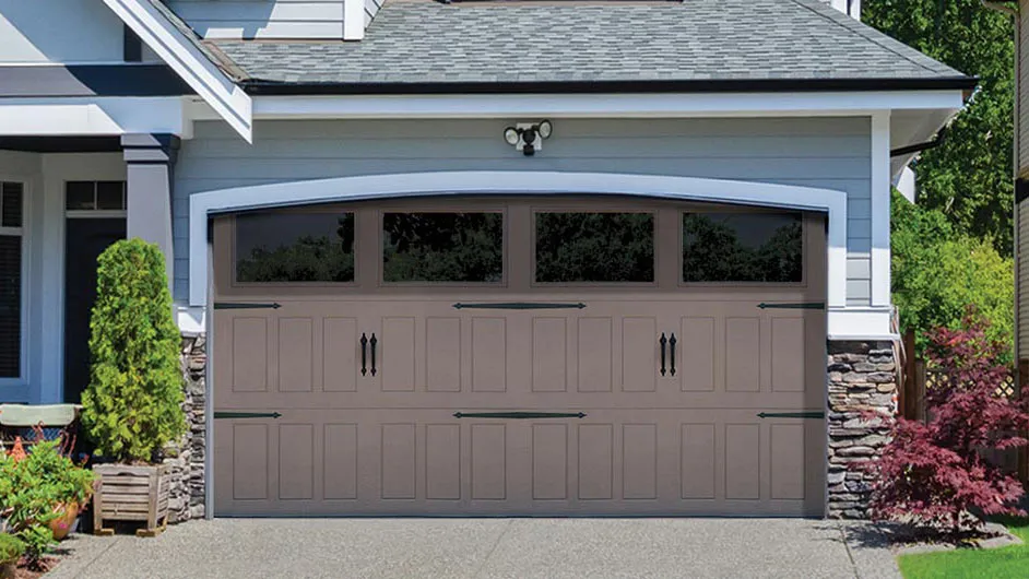 Taupe carriage-house garage door with black hinges, handles, and a row of four tinted glass windows.