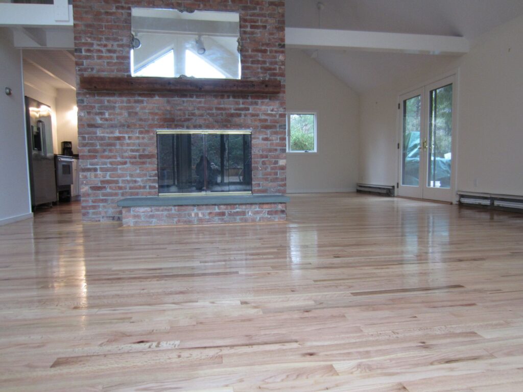 Spacious room with polished hardwood floors, a red brick fireplace, and white French doors.