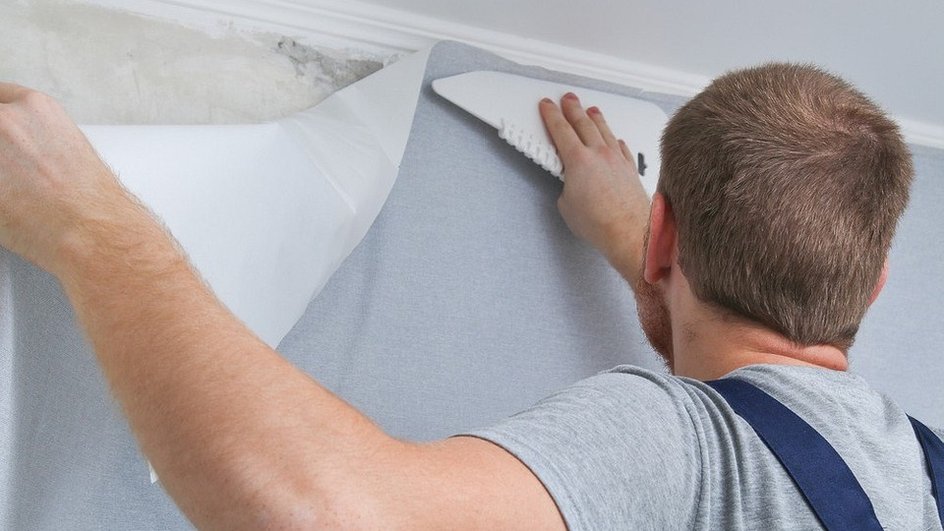 Worker using a plastic smoother to apply wallpaper to a wall.