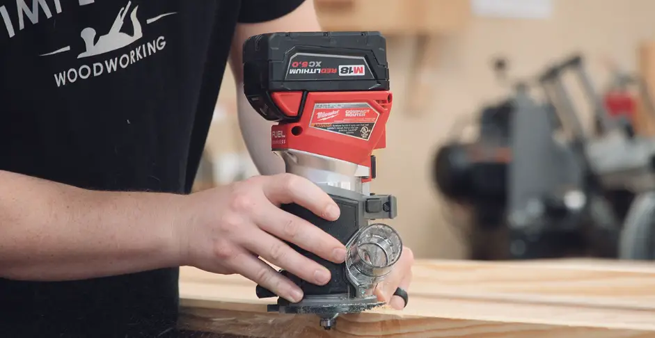 Woodworker using a cordless Milwaukee compact router to shape the edge of a wooden board.