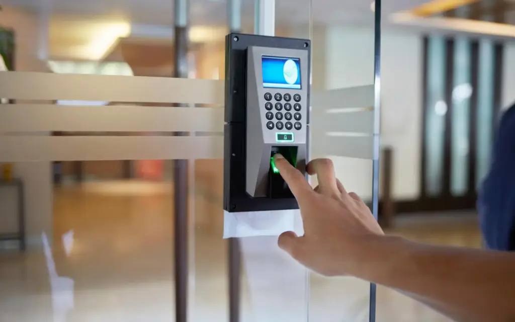 Person using a biometric fingerprint scanner on a security keypad mounted to a glass door.