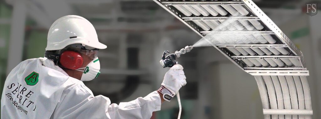 A worker in personal protective equipment spray-coating fire-retardant material onto electrical cable trays.