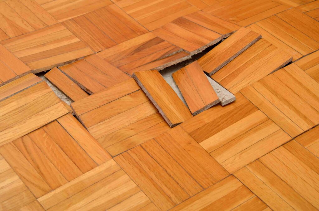 Damaged wooden parquet floor with shifted tiles and gaps.