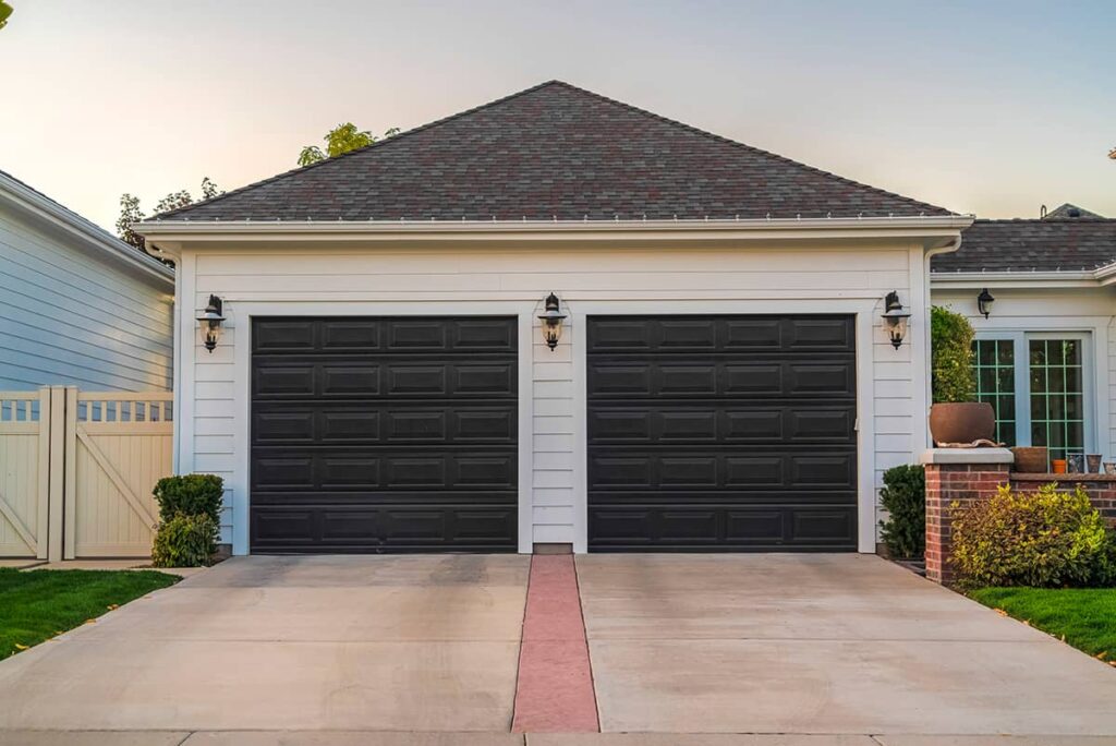 Two-car white garage with dark grey paneled doors and a concrete driveway with a red stripe.