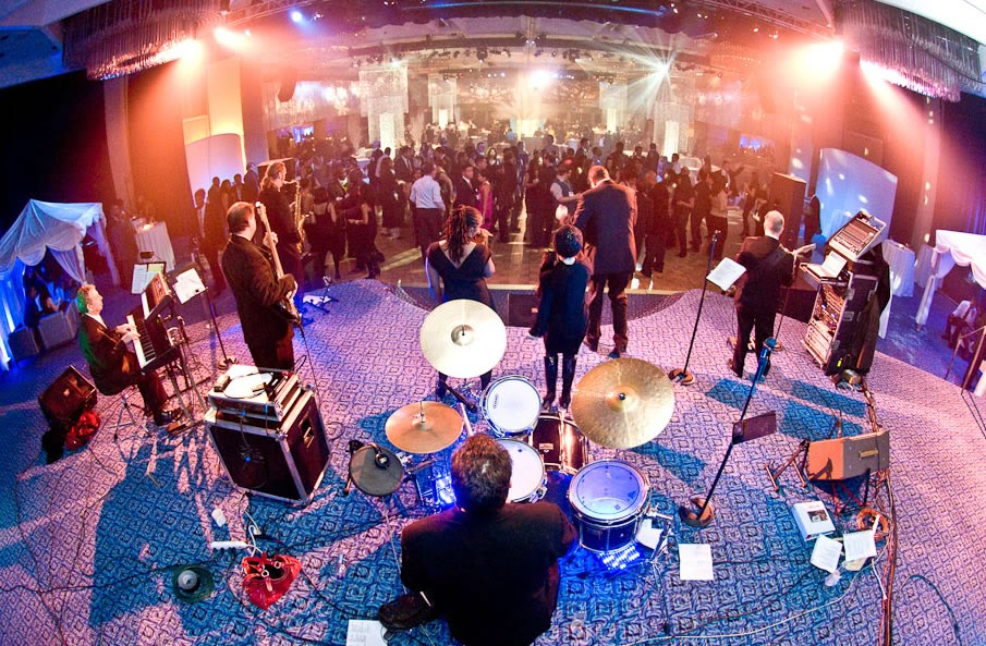 A jazz band performs on a stage overlooking a crowded ballroom at a formal event.
