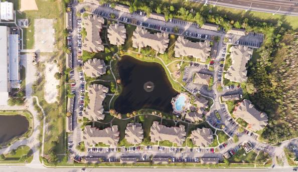 Aerial view of an apartment complex surrounding a central pond, swimming pool, and landscaped green spaces.