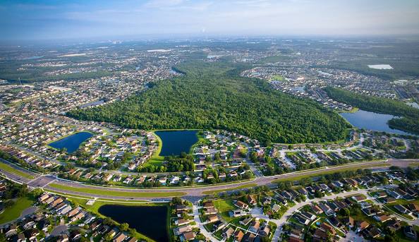 Aerial view of a suburban neighborhood surrounding a large central forest with several small lakes.