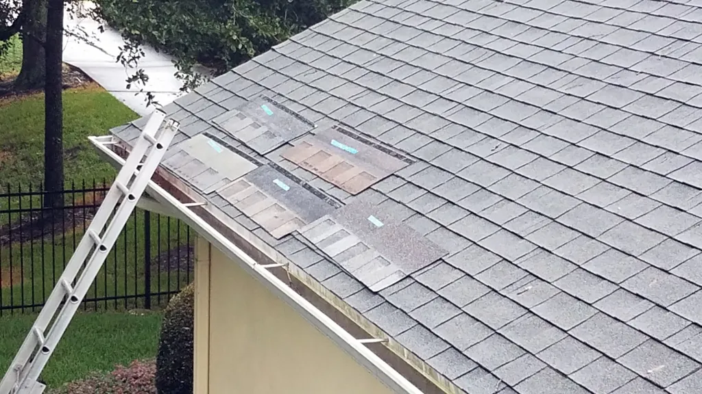 Grey shingled roof with several differently colored sample shingles taped to the surface and a white ladder.