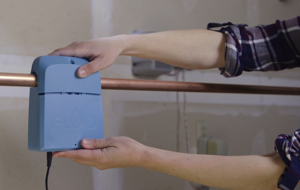 Hands attaching a blue FLOID device to a copper pipe.