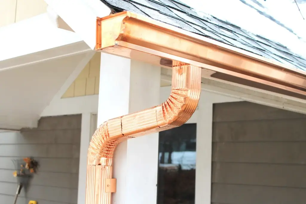 Polished copper gutters and offset downspout attached to a white house column.