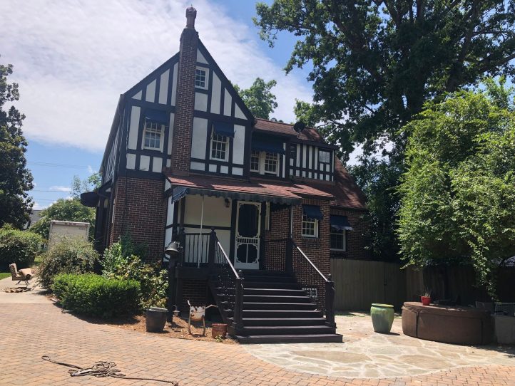 Tudor-style brick and half-timbered house with a prominent chimney and front staircase leading to a covered entryway.