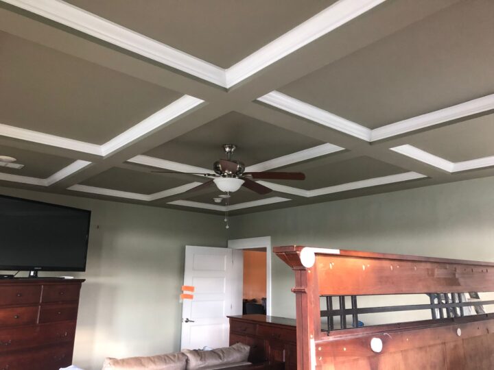 Beige coffered ceiling with white trim and a central ceiling fan in a bedroom.