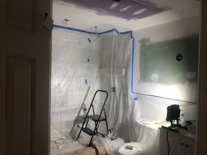 Bathroom under renovation with protective plastic sheeting, a step ladder, and a work light.