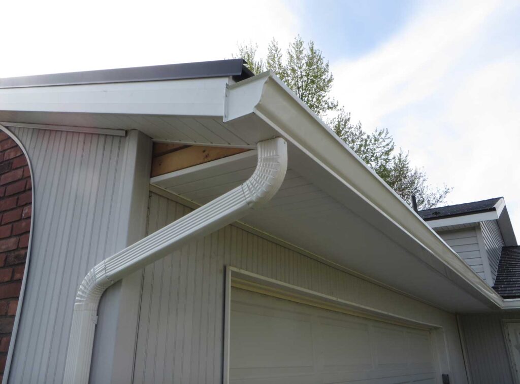 White gutters and a curved downspout installed on a house with light gray siding.