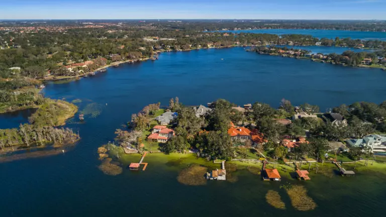 Aerial view of a lush peninsula with luxury waterfront homes, docks, and green lawns surrounded by a large blue lake.