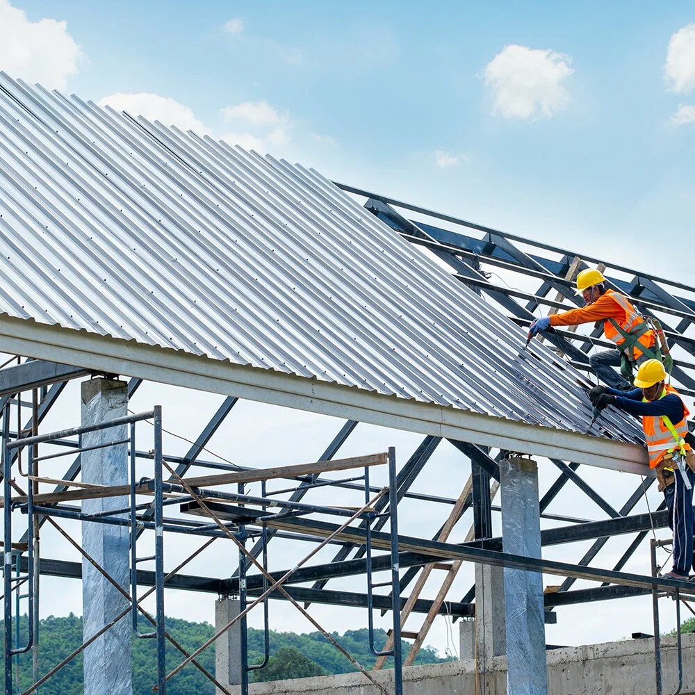 Construction workers in safety gear installing a corrugated metal roof on a steel building frame.