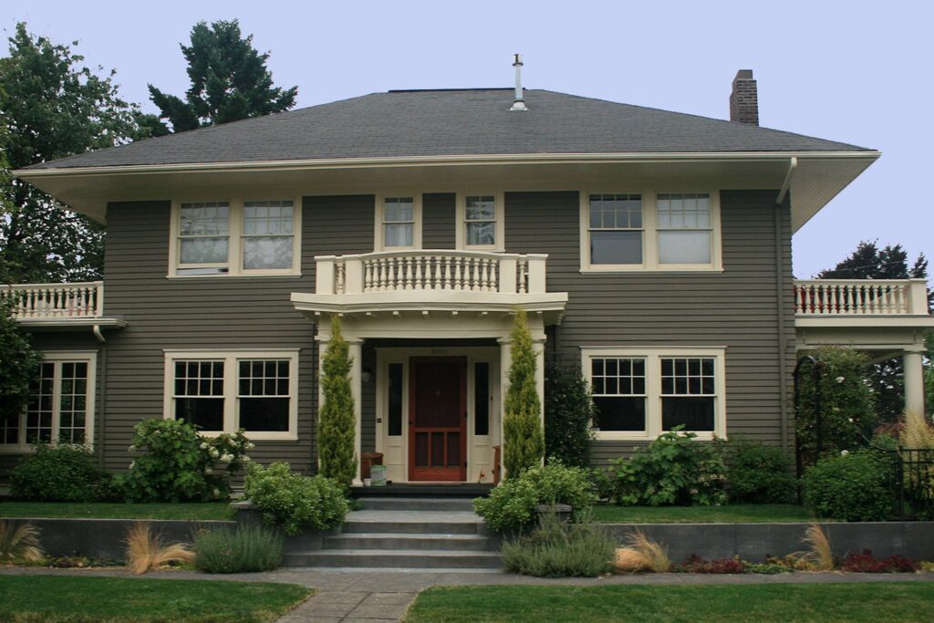 A two-story dark olive home with a prominent front balcony, white trim, and symmetrical landscaping.