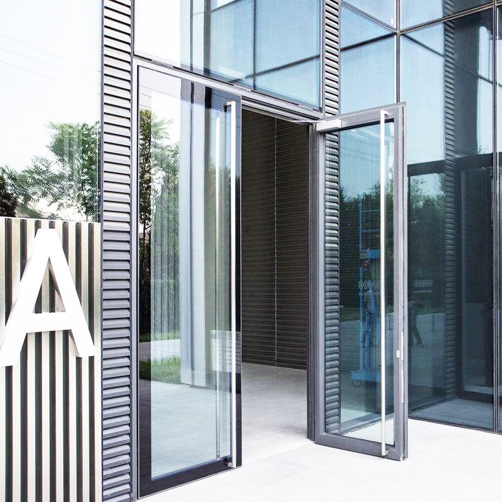 Modern glass building entrance with open doors and a large white letter A on a striped sign.