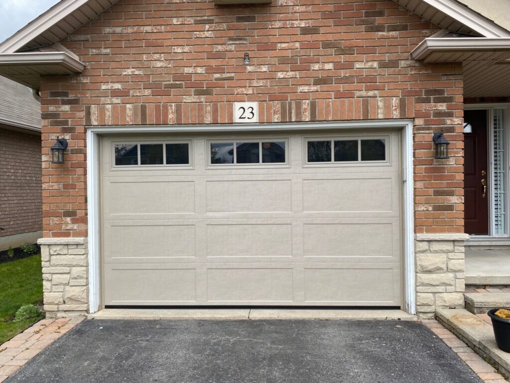 Beige garage door with windows on a red brick house, number 23 above, and black lanterns on each side.