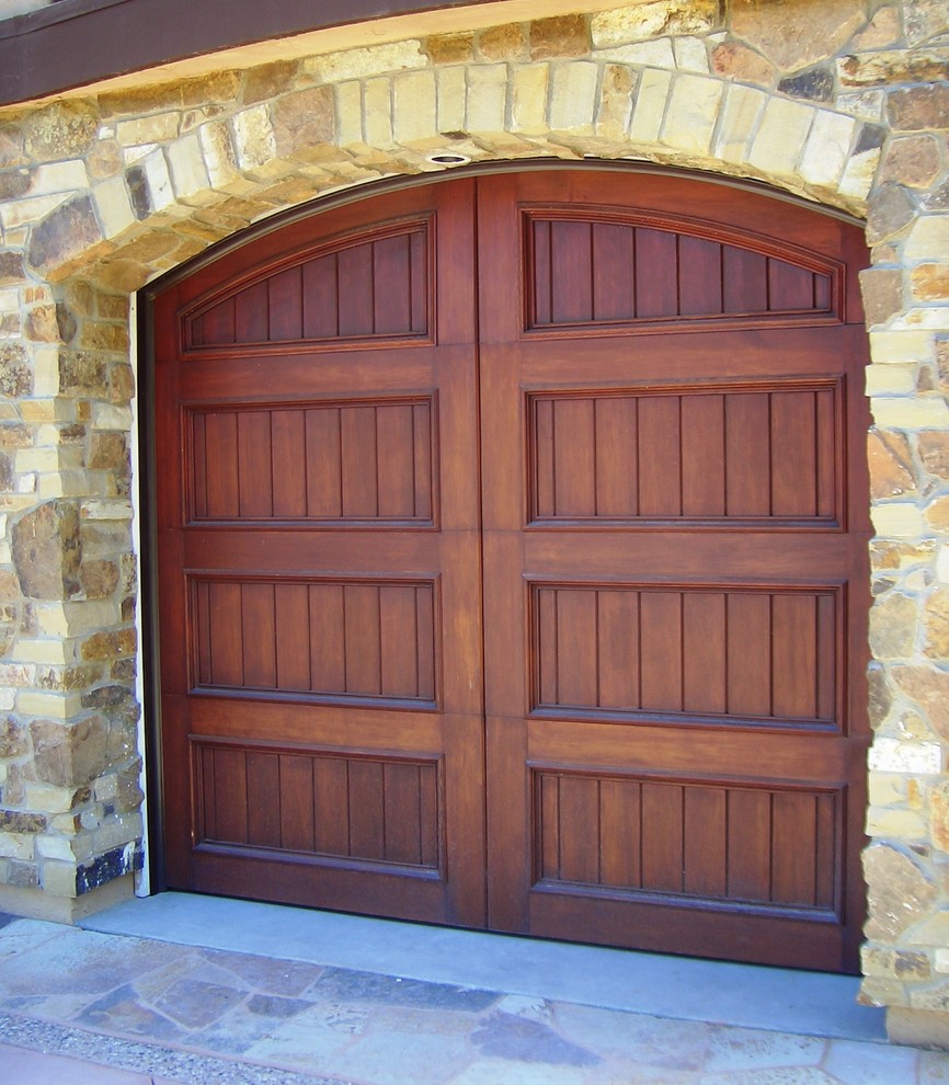 Dark brown arched wooden garage door set within a textured stone wall.