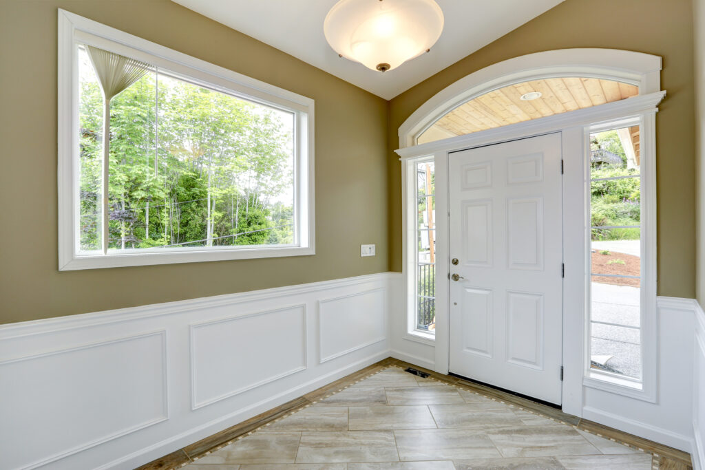 Bright entryway with tan walls, white wainscoting, tiled floors, a large window, and a white front door with side windows.