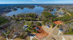 Aerial view of houses near a large lake surrounded by forest, with some cleared lots marked by white boundary lines.
