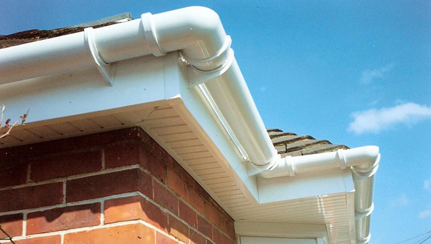 White PVC gutters and downspouts installed on a brick house under a blue sky.