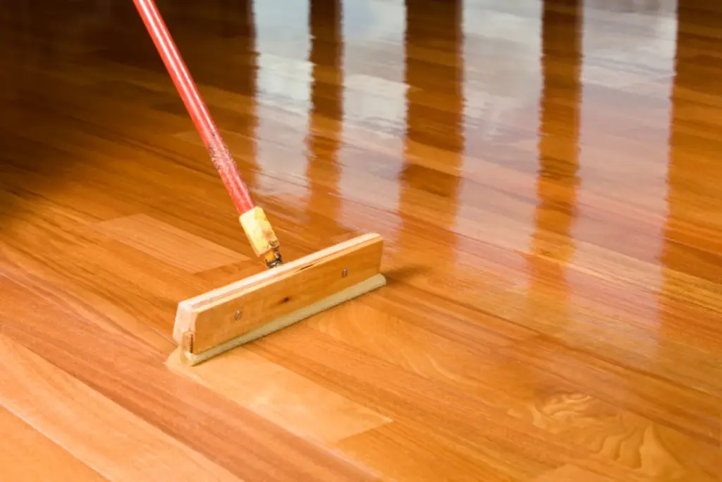 A wooden floor applicator applying a glossy finish to hardwood floorboards.
