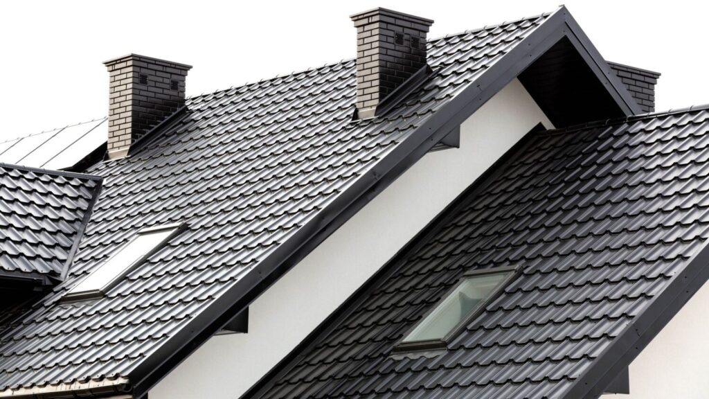 Modern black metal tiled roof with skylights and two grey brick chimneys.