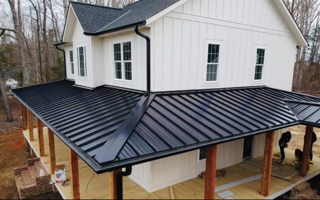 White board and batten house with a black standing seam metal roof on a wrap-around porch.
