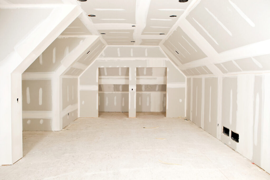 An attic room under construction with bare drywall, taped seams, and recessed lighting installed in the ceiling.