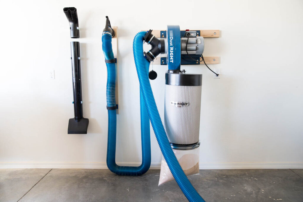 Wall-mounted Dust Right dust collection system with blue hoses, a filter canister, and a detached vacuum nozzle on the wall.
