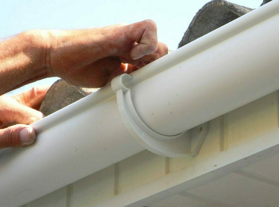 Hands installing a white plastic gutter bracket.