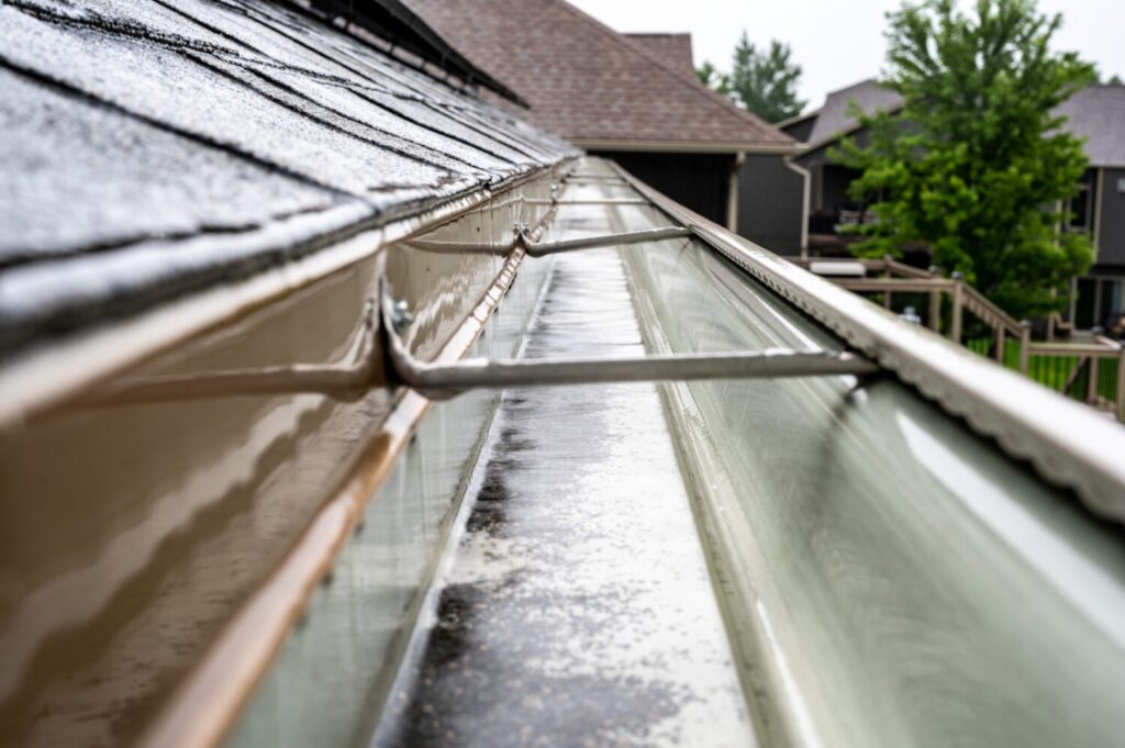 Close-up of a wet residential gutter with installed gutter guards beneath a shingled roof.