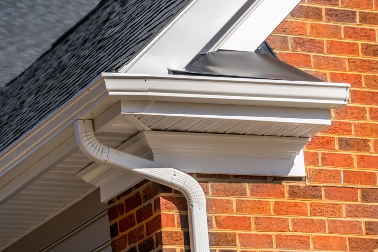 White gutters and downspouts on a red brick house with a grey shingle roof.