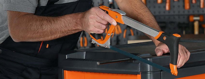 Person using a handsaw to cut the edge of a plastic toolbox.
